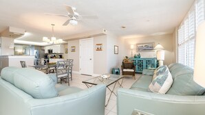 A spacious living room with a dining area, a kitchen in the background, and a view of the outside.