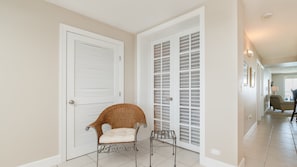 Un couloir avec une chaise en osier et une chaise en métal, des portes blanches à panneaux ajourés et un sol carrelé.