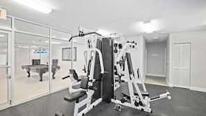 Une salle de sport équipée de matériel d’exercice, avec une table de billard et une table de jeu de fléchettes à l’arrière-plan.