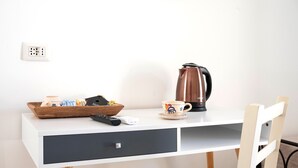 Un bureau blanc avec un tiroir, une télécommande, une cafetière, une tasse et un plateau contenant des collations et une grande tasse.