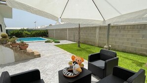 Un espace extérieur aménagé avec une terrasse, une piscine, des coins salon couverts et un petit jardin.