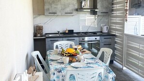 Une cuisine compacte avec un coin repas, comprenant un plan de travail en marbre, une cuisinière à gaz et une table à manger agrémentée d’assiettes, de tasses et d’un panier de fruits.
