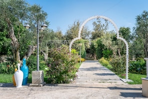 A pathway leading through a garden with a white archway, surrounded by greenery and decorative vases. - Room 'San Biagio - Superior 102' with Shared Pool, Wi-Fi and Air Conditioning (Calimera)