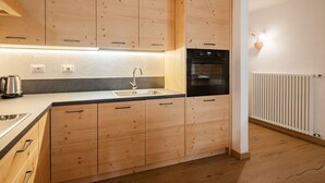 Una cucina moderna con mobili in legno, un lavello in acciaio inox, un forno nero e un termosifone bianco.