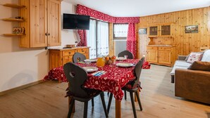 Una camera accogliente con un tavolo da pranzo per quattro persone, armadietti in legno, una televisione e una finestra con tende rosse.