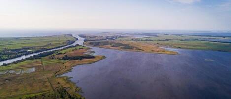 An aerial view of a river winding through a landscape with fields and a distant horizon.