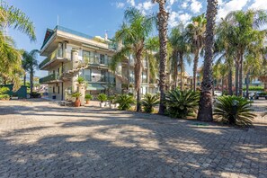 A multi-story building with balconies, palm trees, and a paved courtyard.