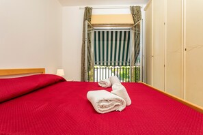 Une chambre d’hôtel avec un lit, une fenêtre avec des rideaux, un balcon et une armoire.