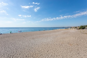 Une vaste plage de sable, parsemée de parasols, un ciel d égagé et une côte lointaine.