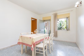 Un coin repas avec une table dressée pour quatre personnes, une porte donnant sur l’extérieur et une fenêtre offrant une vue sur la verdure.