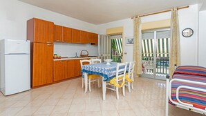 A compact kitchen with wooden cabinets, a white refrigerator, and a dining table with chairs. - Apartment 'I Ciottoli Dello Ionio - Apt 15' with sea view, shared terrace and balcony (Mascali)