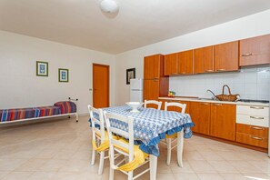 Uma cozinha compacta com armários de madeira, uma mesa de jantar com cadeiras e uma cama pequena no canto.