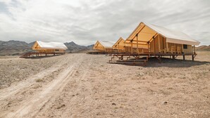A row of wooden cabins with elevated platforms and open sides, set in a dry, mountainous landscape. -  Pana Unique Charyn (Charyn Canyon)