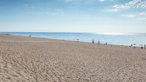 A beach with a clear sky, a sandy shore, and umbrellas.