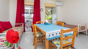 A room with a bed, a table with chairs, a red curtain, and a clock on the wall.