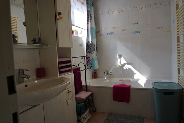 A bathroom with a sink, mirror, bathtub, and a shower curtain with fish patterns.