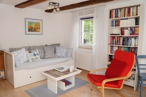Un saló amb un sofà blanc, una cadira vermella, una estanteria i una finestra amb cortines.