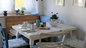 Uma área de refeições com uma mesa posta para dois, uma janela com cortinas e uma parede com utensílios pendurados.