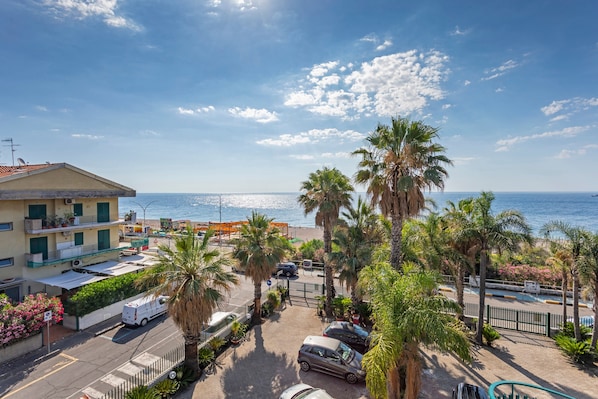 Un quartier résidentiel situé sur la côte, avec vue sur la mer, des voitures garées et des palmiers.