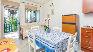 Une pièce comprenant une table à manger, des chaises, un coin cuisine, un balcon avec vue sur la verdure et une porte coulissante.