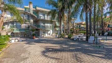A courtyard with a cobblestone ground, palm trees, outdoor seating, and a multi-story building with balconies.