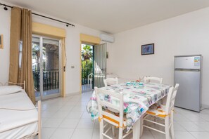 Una habitación con cama, una mesa de comedor con sillas, un refrigerador y un ventanal corredero que da a un espacio al aire libre.