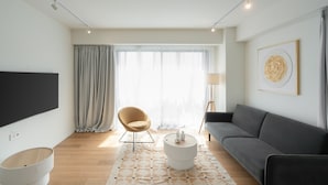 Een moderne woonkamer met een bank, een fauteuil, een salontafel, een televisie en een raam met gordijnen.