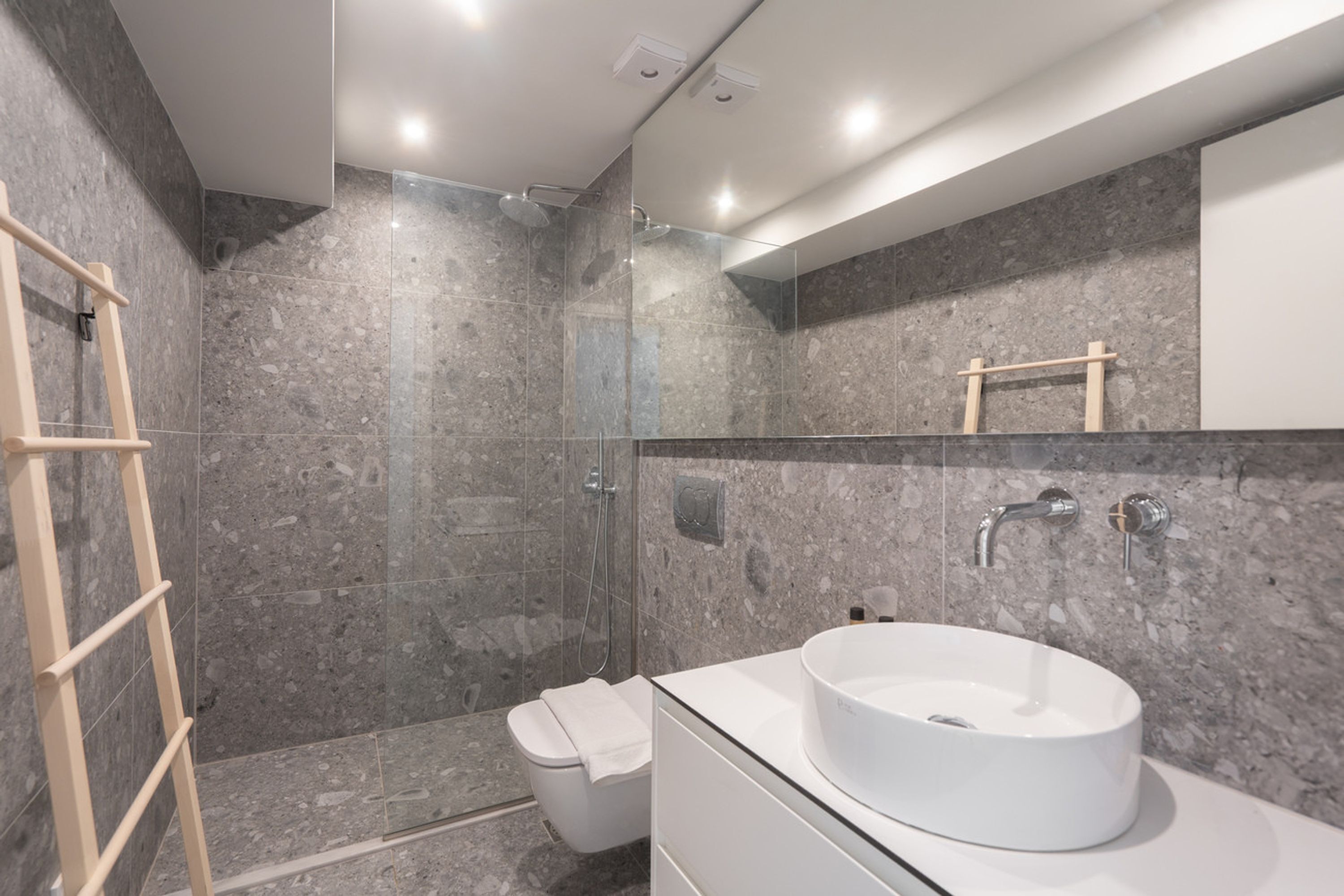 A modern bathroom with a glass-enclosed shower, a white sink, and a wooden ladder.