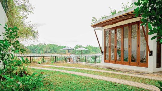 A modern building with large glass doors, a covered outdoor seating area, and a view of a body of water. - The Rivergates Villa (Panadura)