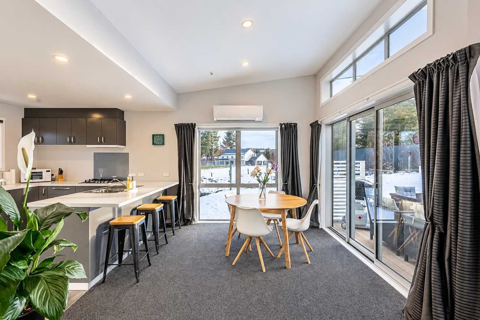 A modern kitchen with a dining area, large windows, and a view of the outside.
