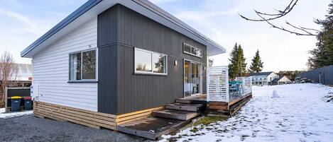 A modern two-story house with a flat roof, large windows, and a wooden deck.