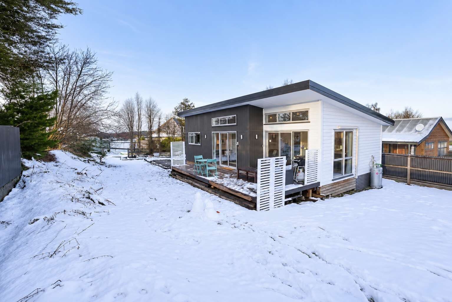 A modern two-story house with a covered patio and a snow-covered yard.