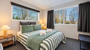 A hotel room with a bed, two bedside tables, a lamp, a window with curtains, and a view of trees.