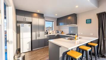 A modern kitchen with grey cabinets, a stainless steel refrigerator, a microwave, and a sink. There are three stools at the island.