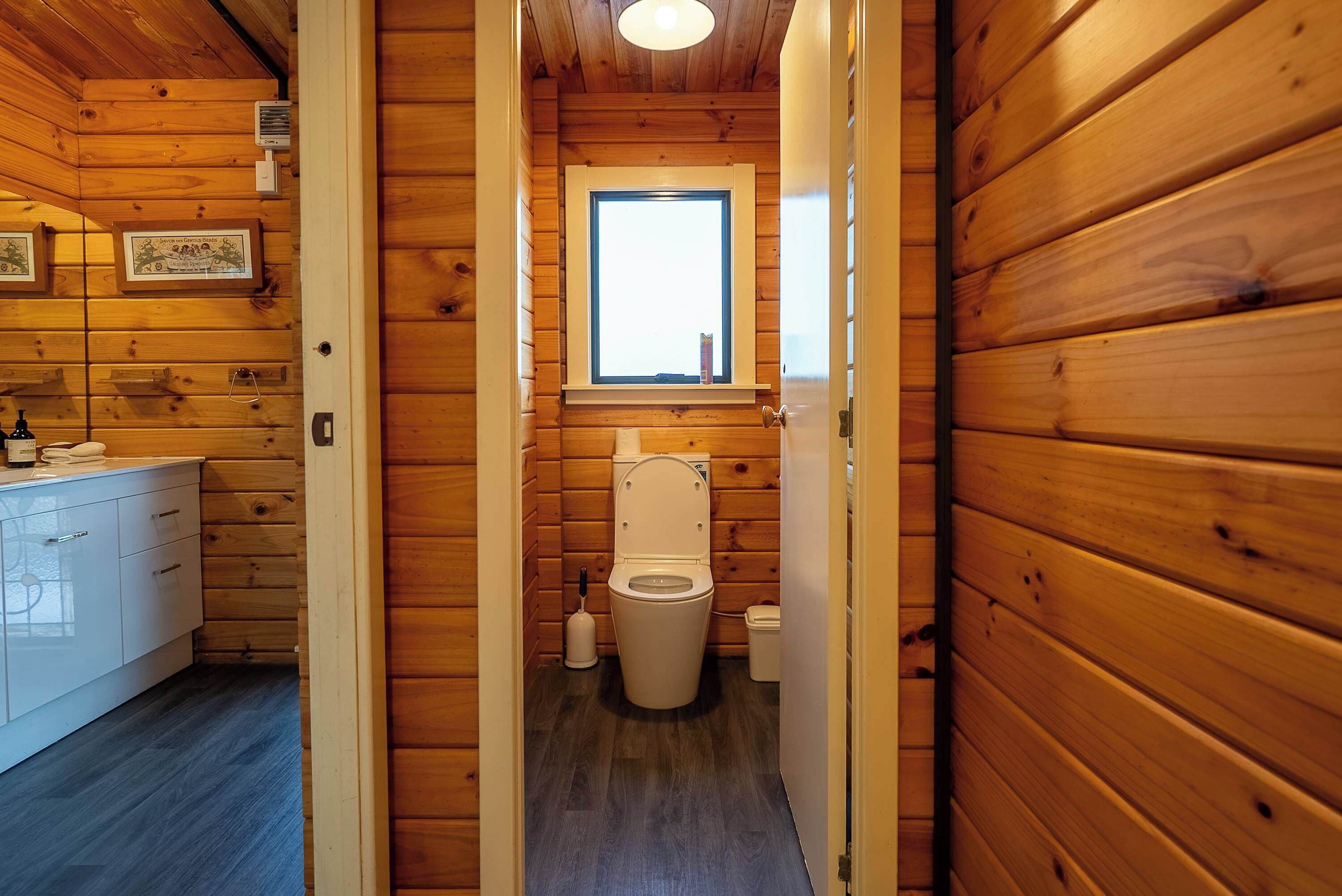 Un bagno in una cabina di legno, con il water, una finestra e un lavabo con mobili.