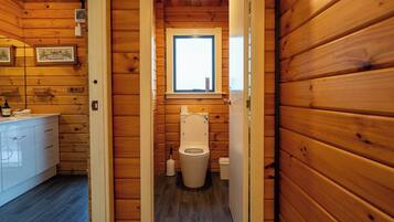 Un bagno in una cabina di legno, con il water, una finestra e un lavabo con mobili.