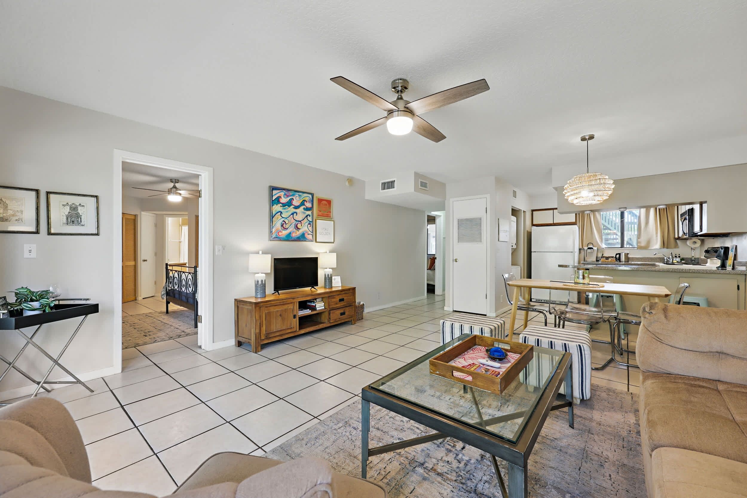 A spacious living room with a glass coffee table, a ceiling fan, and a television on a wooden stand.