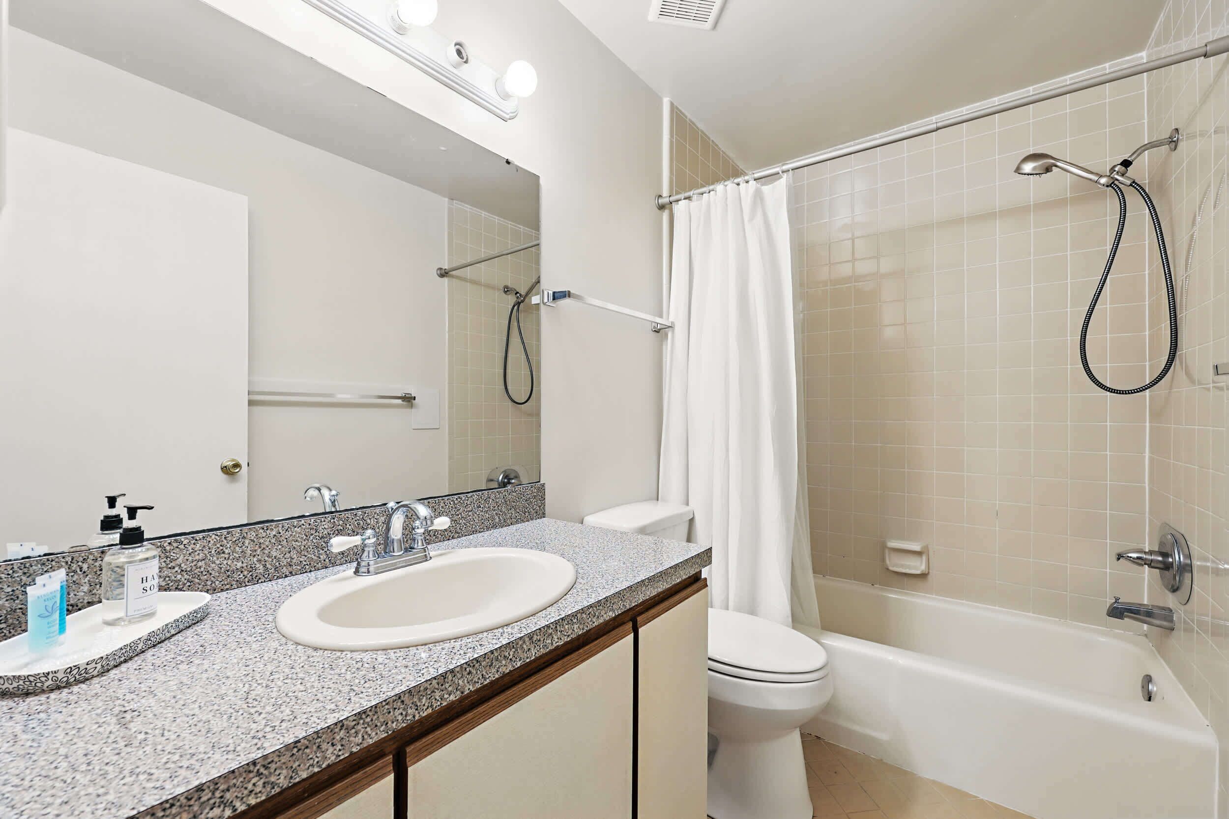 A bathroom with a sink, mirror, toilet, and shower.