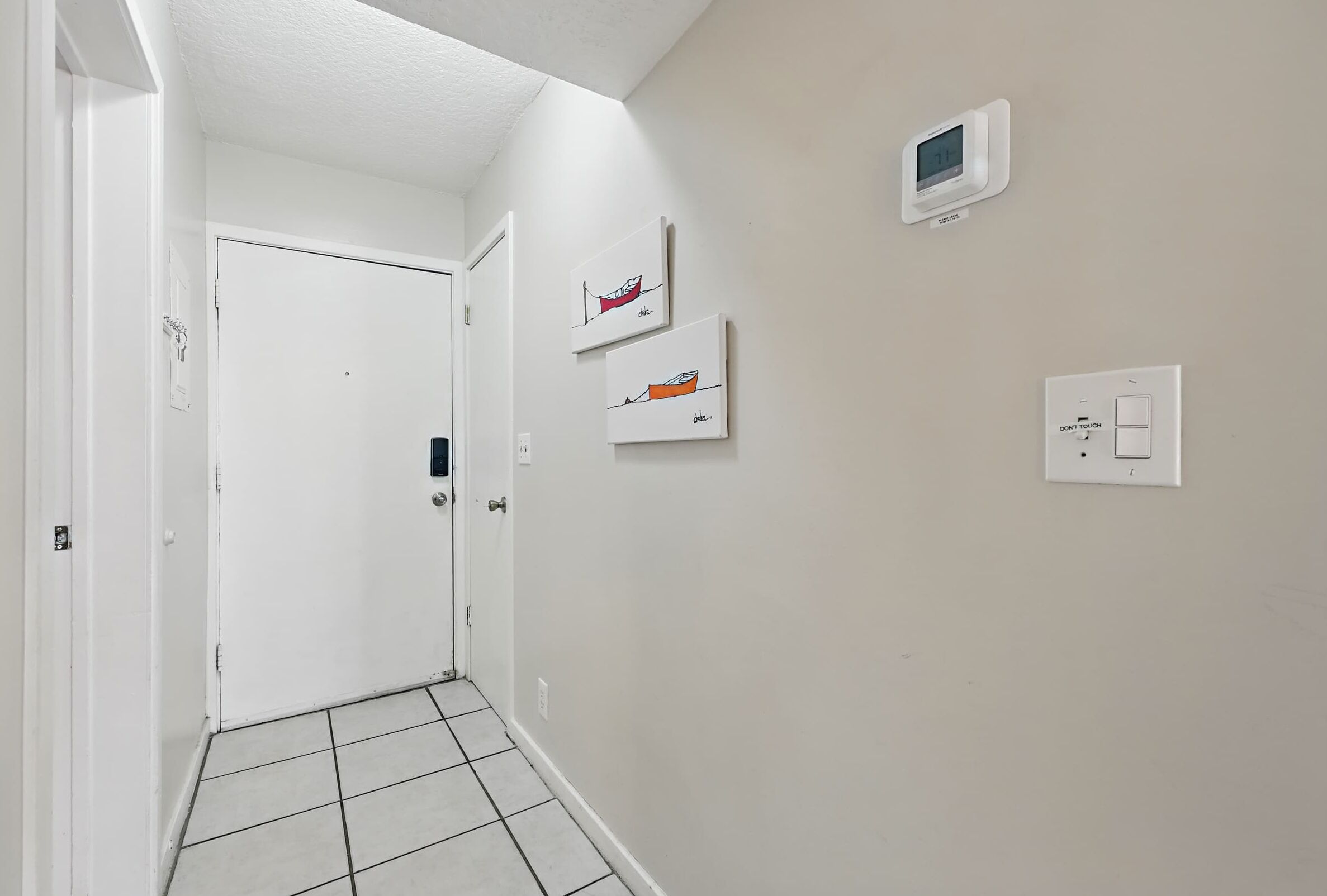 A hallway with a white door, a thermostat, and two framed artworks on the wall.