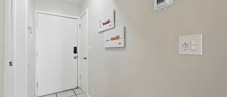 A hallway with a white door, a thermostat, and two framed artworks on the wall.