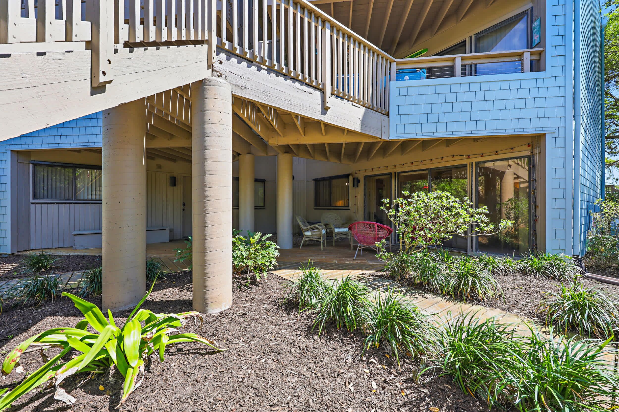 Un espacio al aire libre techado con un conjunto de asientos, un pequeño jardín y un edificio con balcón.