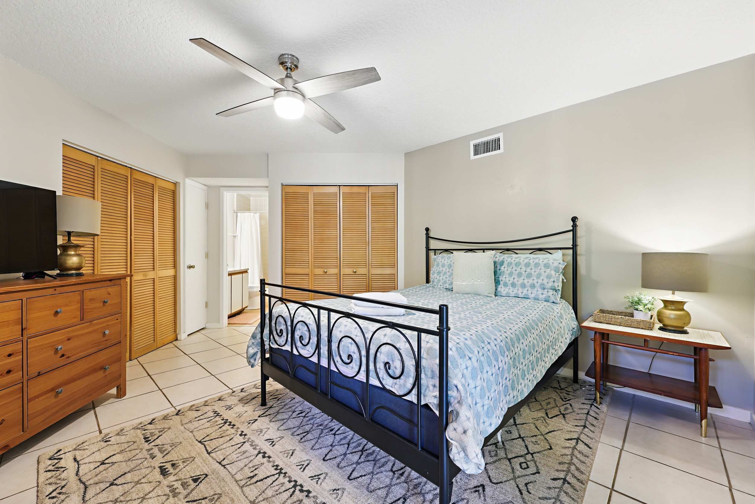 A bedroom with a bed, a dresser, a nightstand, a ceiling fan, and wooden closets.