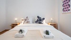 Un lit bien fait, avec du linge de lit blanc, deux tables de chevet avec des lampes et une œuvre d’art abstraite accrochée au mur.