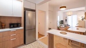 Une cuisine moderne avec des meubles blancs, un réfrigérateur en acier inoxydable et un four à micro-ondes. On y trouve également un coin repas avec une table et des chaises blanches.
