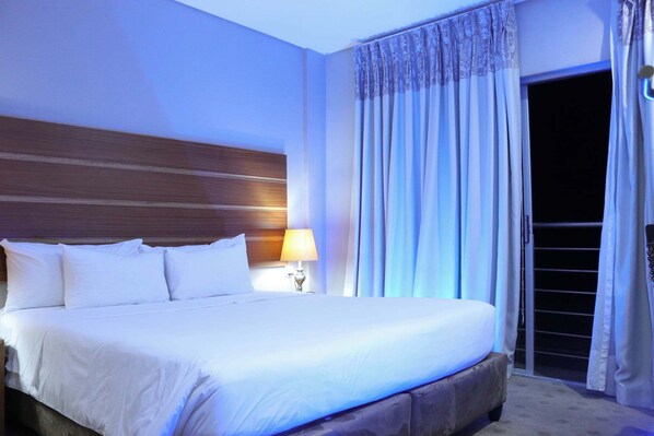 A large bed with white linens, a wooden headboard, and a nightstand with a lamp. - Woodlane Hotel (Gaborone)