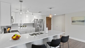 A modern kitchen with white cabinetry, stainless steel appliances, a central island with seating, and pendant lighting. - Private Condo | CDGA Lake | Seasonal Hot Tub/Pool (Canandaigua)