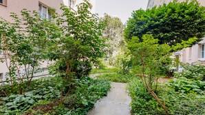 Un sendero estrecho bordeado por abundante vegetación y edificios con balcones.