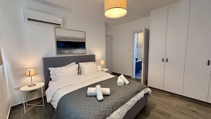Een moderne slaapkamer met een groot bed, nachtlampen, een schilderij en een kledingkast.