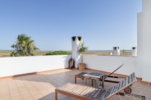 A terrace with a view of the sea, a palm tree, and a traditional windcatcher.