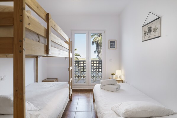 A room with two single beds, a wooden bunk bed, a sliding glass door leading to an outdoor area, and a framed picture on the wall.